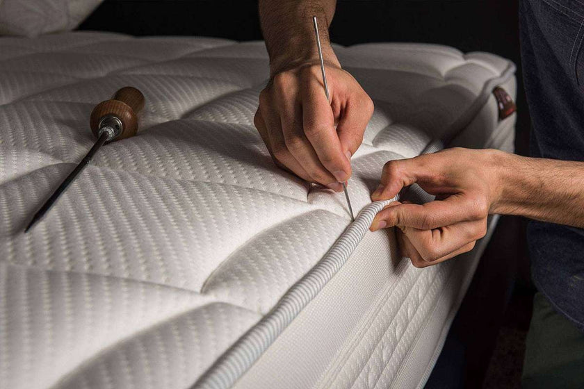 A craftsperson hand-finishing a mattress
